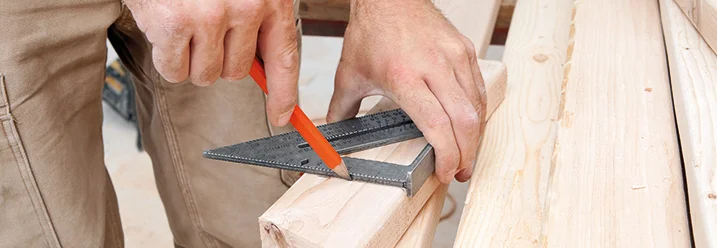 Person misst Holzbrett mit Winkel